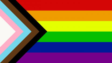 Progress Pride flag, including original rainbow design, trans flag elements and black and brown stripes for racial justice.